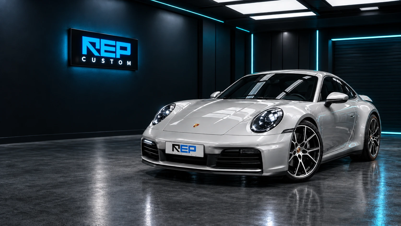 Porsche 911 prateado na oficina da REP Custom, com a marca iluminada na parede.