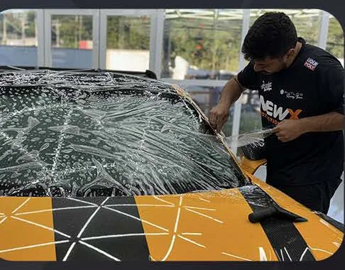 Aplicador posiciona a película Windshield no para-brisa de um carro amarelo.